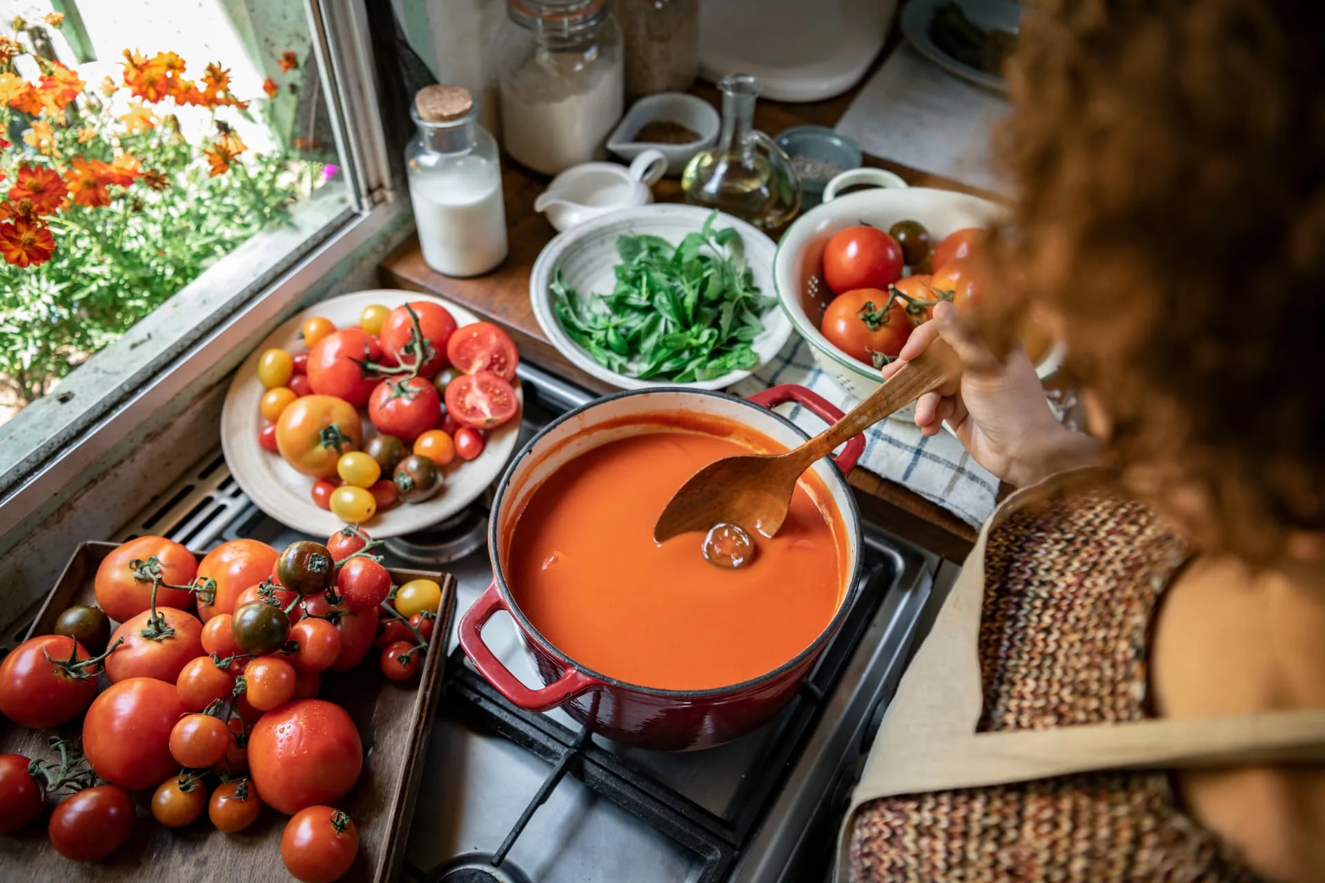 Tomato soup cooking in a red pot beside fresh tomatoes